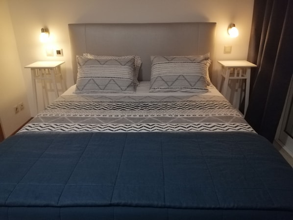 A bed with a geometric patterned bedspread and two pillows, flanked by bedside tables with wall-mounted lamps.