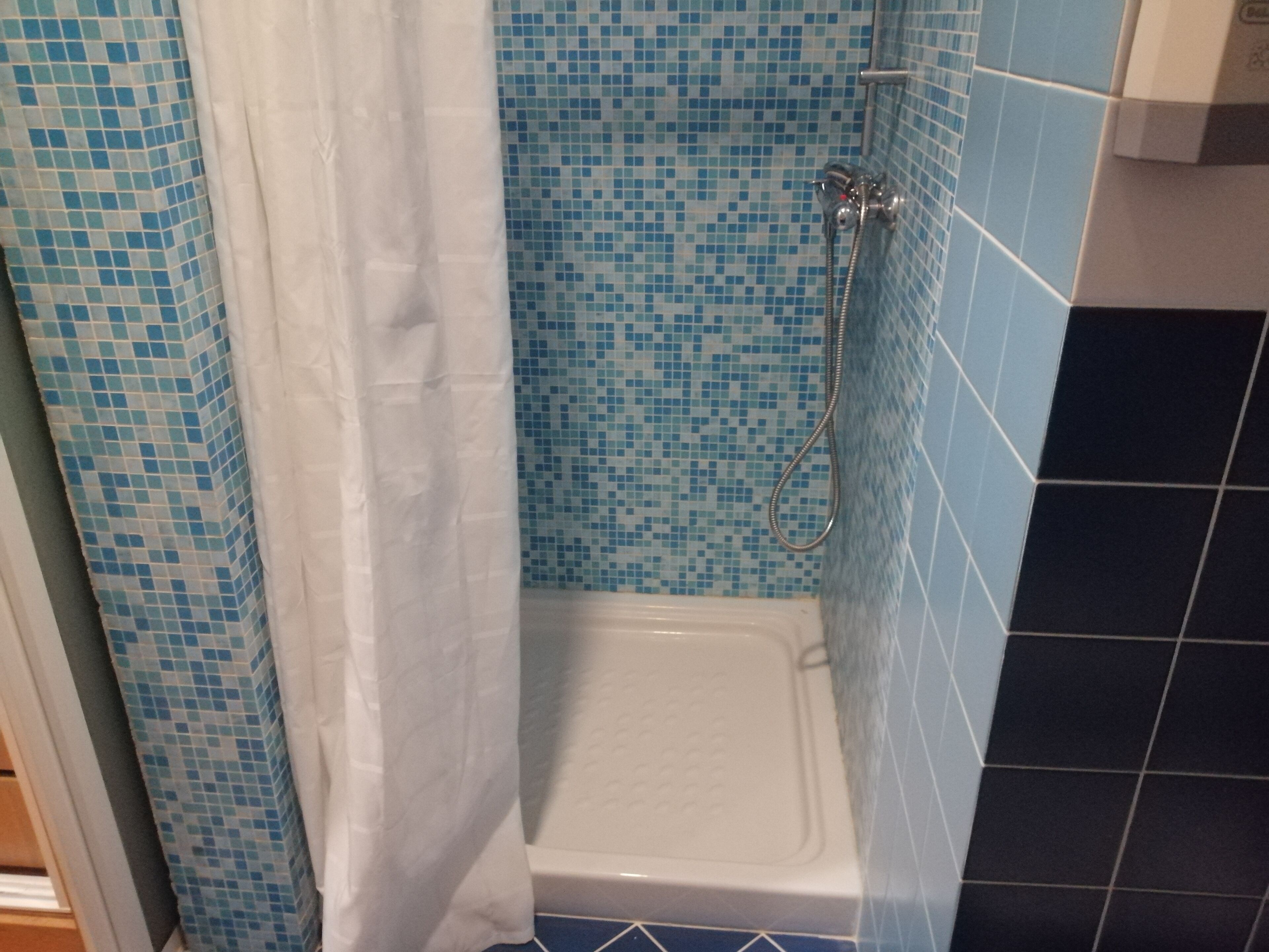 A bathroom with a shower, tiled walls, and a white bathtub.