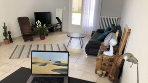 A living room with a laptop on a table, a sofa, a chair, a television, and a radiator. - LA Villa Avignon - Centre Ville - Piscine Privée - Intramuros (Avignon)