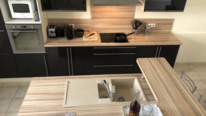 A modern kitchen with a wooden countertop, built-in oven, microwave, and a sink with a wine bottle and glasses on the counter. - LA Villa Avignon - Centre Ville - Piscine Privée - Intramuros (Avignon)