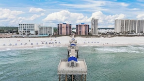 Une jetée qui mène à une plage, bordée de parasols, avec une vue sur la ville en arrière-plan.