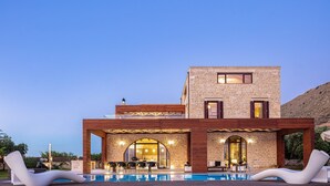 A modern building with a pool, lounge chairs, and a covered patio area.