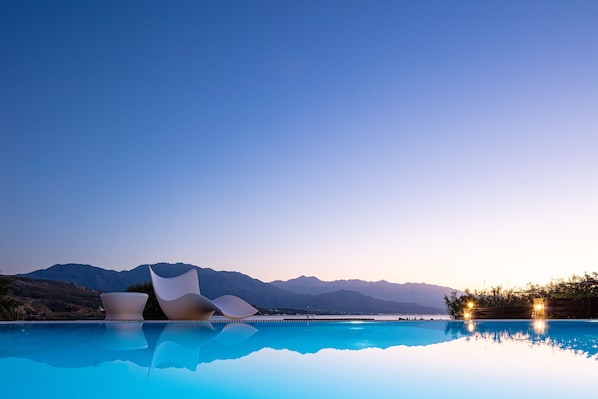 A pool with modern chairs and a mountain backdrop.