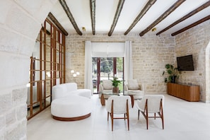 A spacious living area with a stone wall, a glass coffee table, white sofas, and wooden chairs.