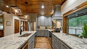 A modern kitchen with granite countertops, stainless steel appliances, and a wooden ceiling. - Forest Home|5B/5.5BA|Hot tub|Game Room|Playset (Broken Bow)