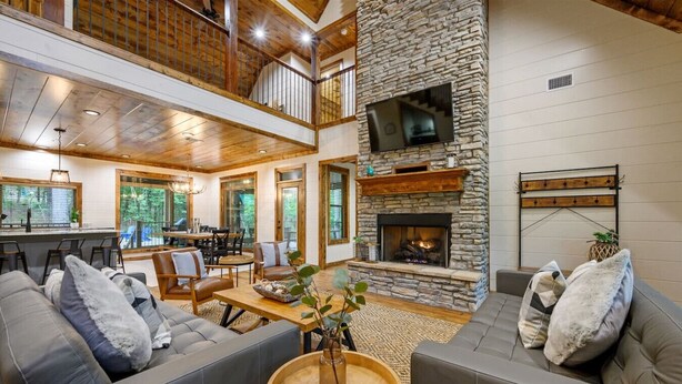 A spacious living area with a stone fireplace, a dining area, and a kitchen. - Forest Home|5B/5.5BA|Hot tub|Game Room|Playset (Broken Bow)
