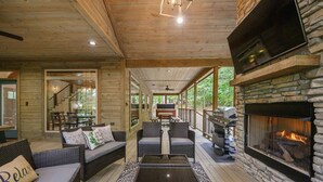 A covered outdoor area with wicker furniture, a stone fireplace, and a grill. - Forest Home|5B/5.5BA|Hot tub|Game Room|Playset (Broken Bow)