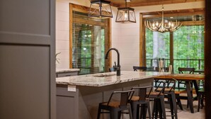 A kitchen with a large island, bar stools, and a dining table. - Forest Home|5B/5.5BA|Hot tub|Game Room|Playset (Broken Bow)