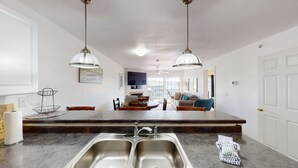 Eine moderne Küche mit Kochinsel, zwei Spülen, Pendelleuchten und einem Essbereich mit einer Couch und Stühlen.