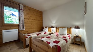 A bedroom with two wooden beds, a window with curtains, a radiator, and a small bedside table with a lamp.