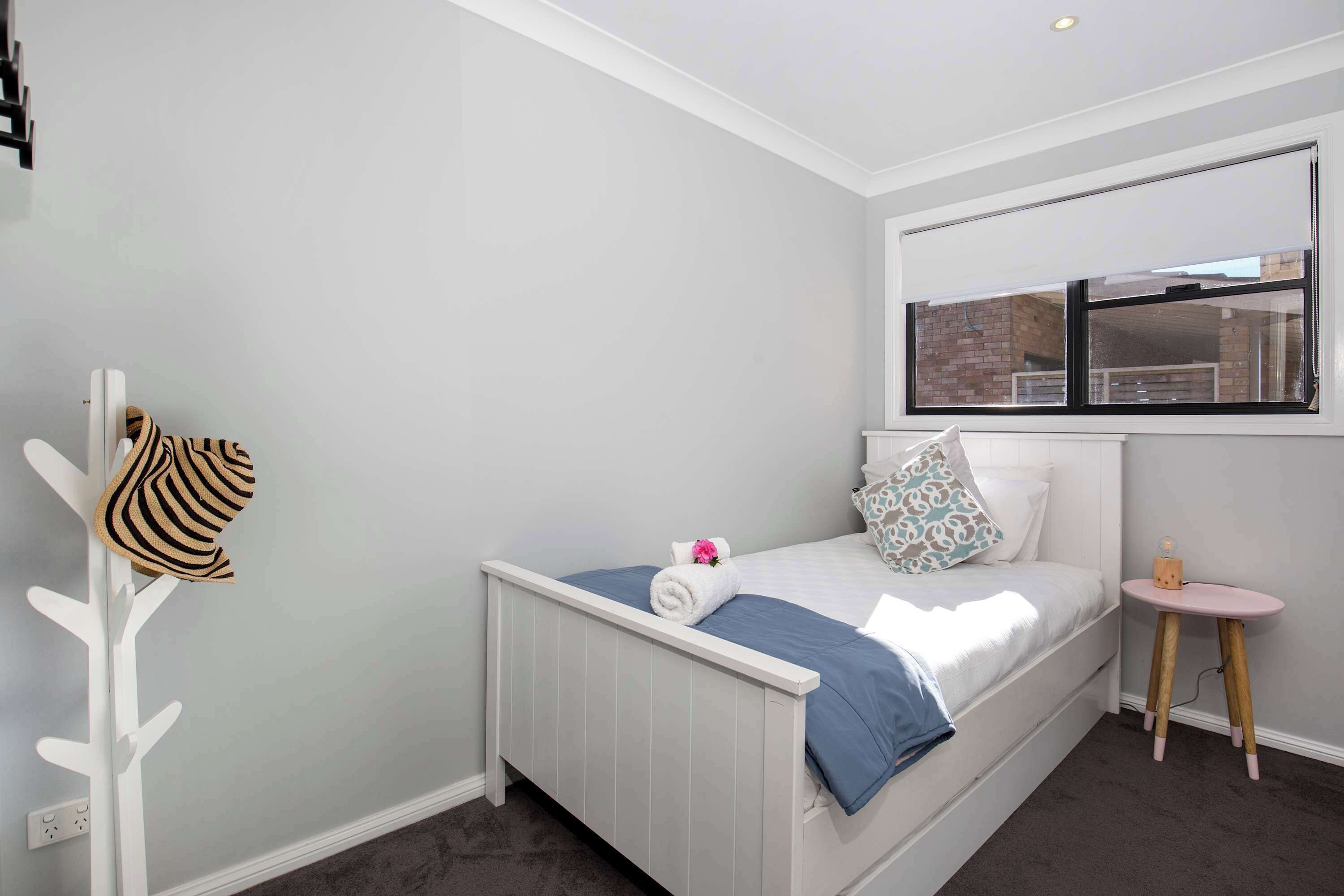 A bedroom with a bed, a window, a small table, and a coat rack.