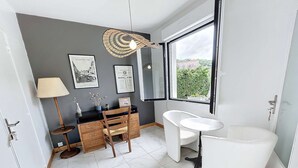 A modern bathroom with a white sink, a freestanding bathtub, a wooden vanity, and a large window offering a view of greenery.
