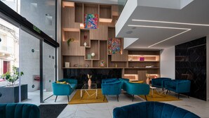 A modern interior with teal sofas, a marble floor, and a wooden shelving unit with artwork. -  Flamingo Hotel (St. Julian's)