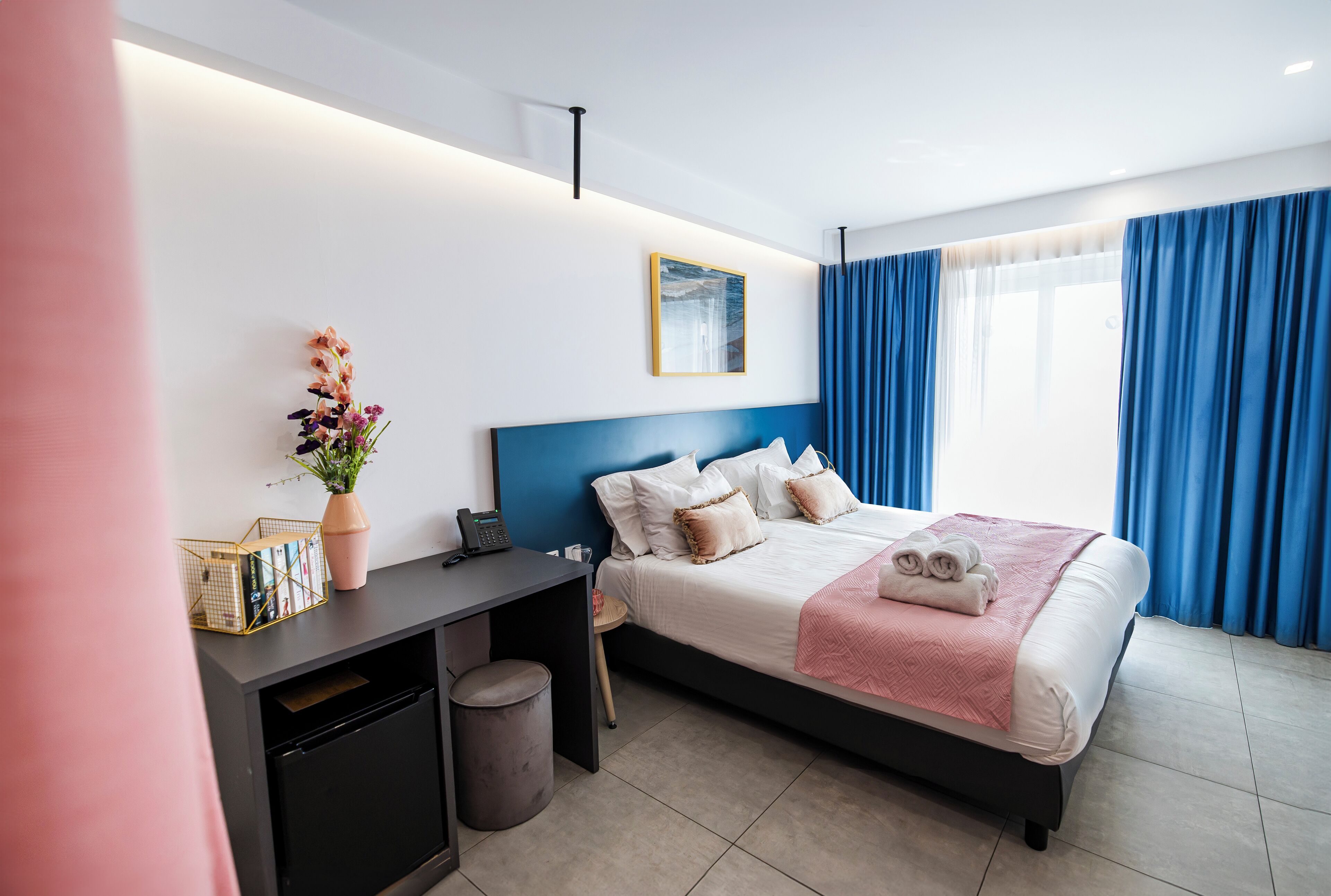 A modern hotel room with a bed, desk, and a small trash bin.