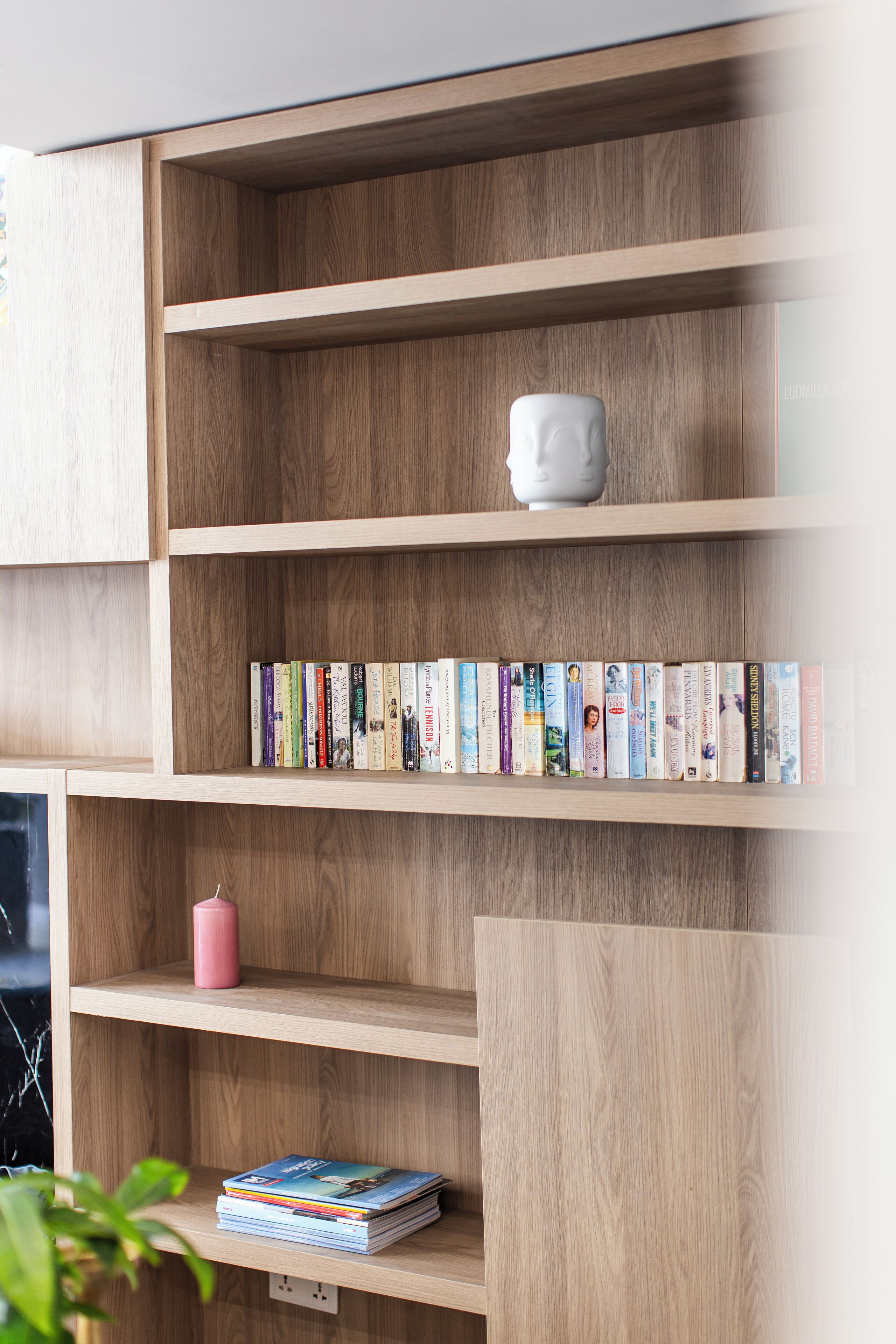 A wooden bookshelf with multiple shelves, some containing books and a pink candle.
