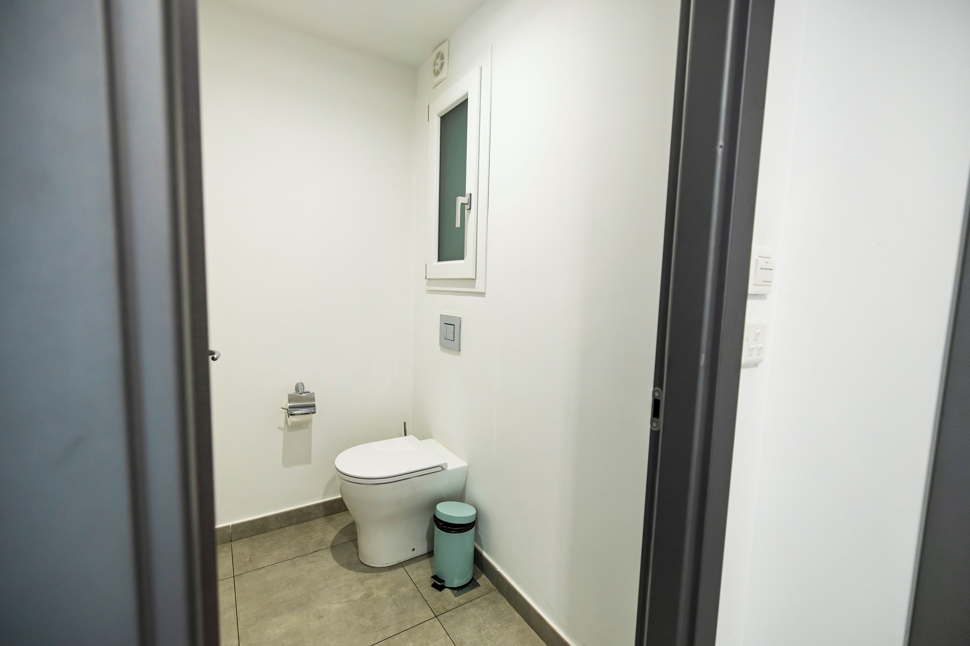 A small, clean bathroom with a toilet, a trash bin, and a wall-mounted mirror.