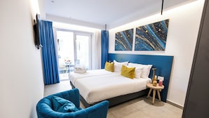 A modern hotel room with a large bed, a blue armchair, and a view of the outside. -  Flamingo Hotel (St. Julian's)