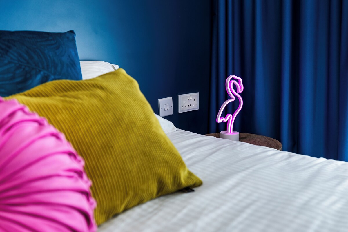 Quarto de hotel com cama, um letreiro de flamingo neon e uma tomada na parede.