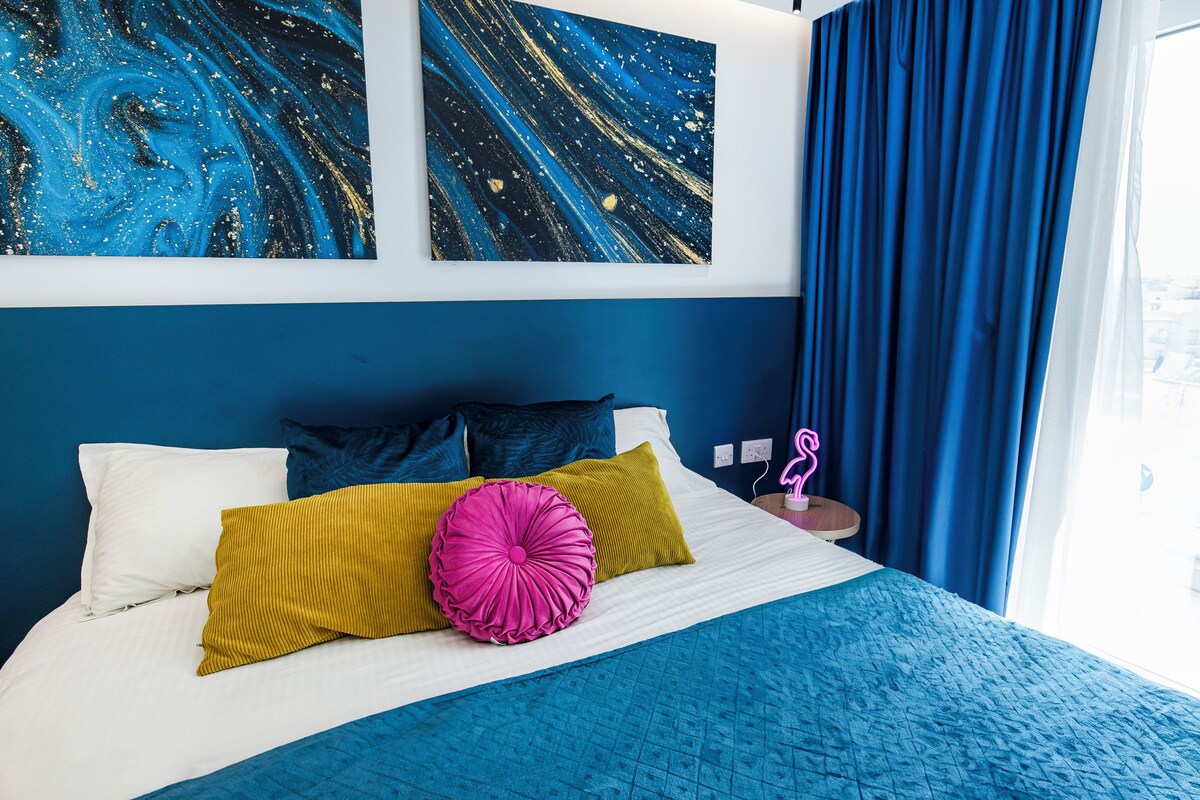 A bed with white and blue bedding, a yellow and pink pillow, and a blue headboard.