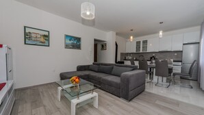 A modern living room with a grey sofa, a glass coffee table with fruit, and a kitchen in the background. - Spacious apt With Lodge Just 40m From the Beach (Kastela)