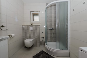 Un baño moderno con ducha de vidrio, inodoro y una pequeña ventana sobre el lavamanos.