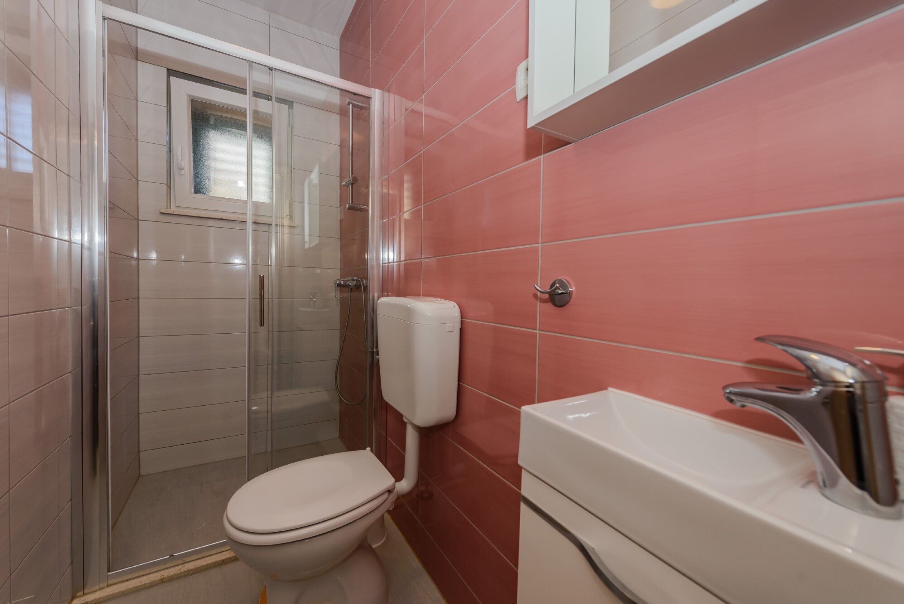 Un baño con cabina de ducha de vidrio, un inodoro blanco y un lavamanos con grifo cromado.