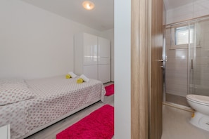 Un dormitorio con cama, armario y baño con inodoro y ducha.