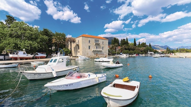 A marina with several boats docked, a stone building with a red roof, and a clear blue sky with scattered clouds. - Spacious apt With Lodge Just 40m From the Beach (Kastela)