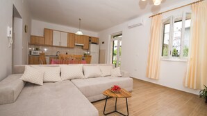 Ein Wohnzimmer mit einem beigefarbenen Ecksofa, einem Holztisch und einer Küche im Hintergrund.