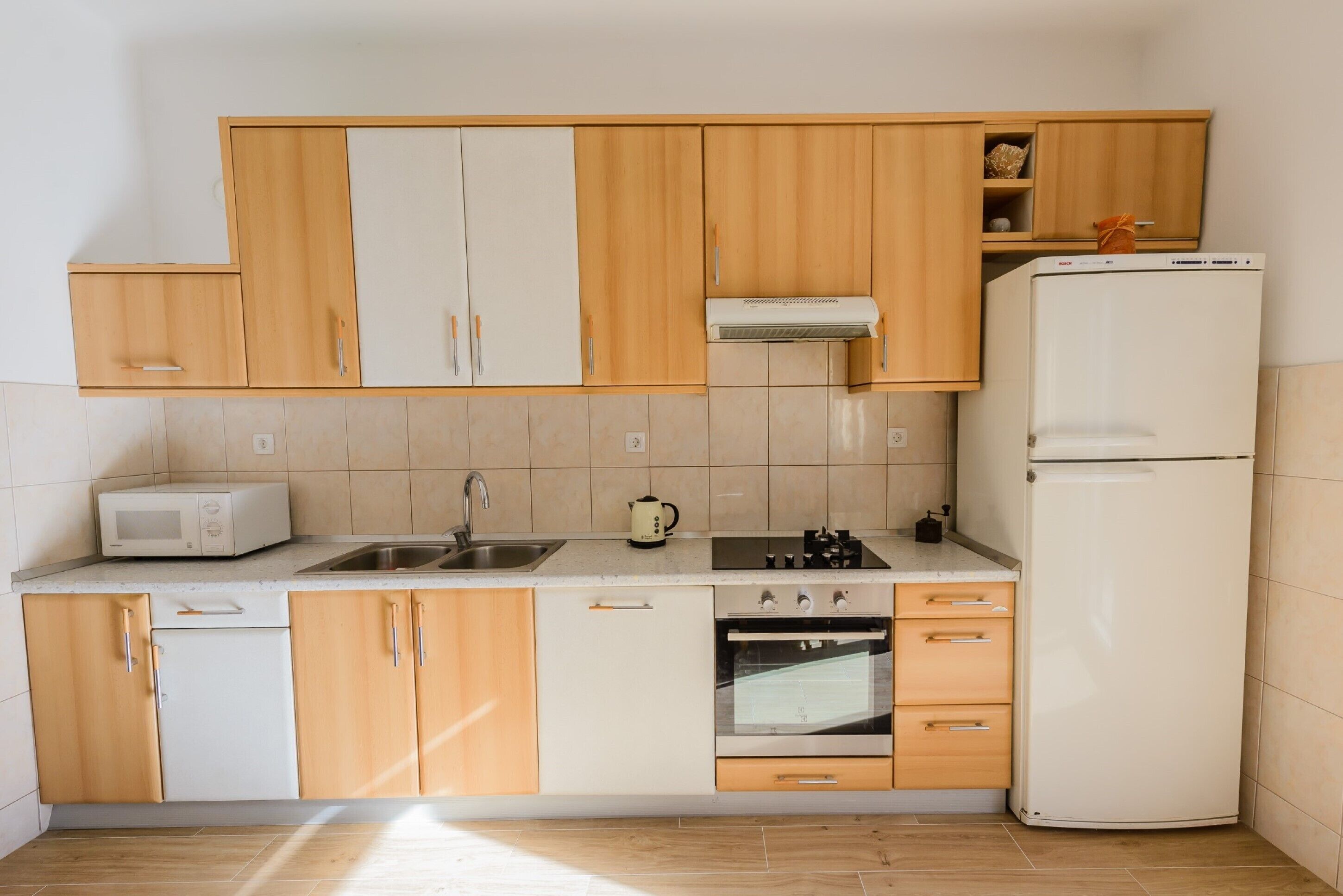 Een compacte keuken met houten kastjes, een witte koelkast, een magnetron, een spoelbak en een oven.