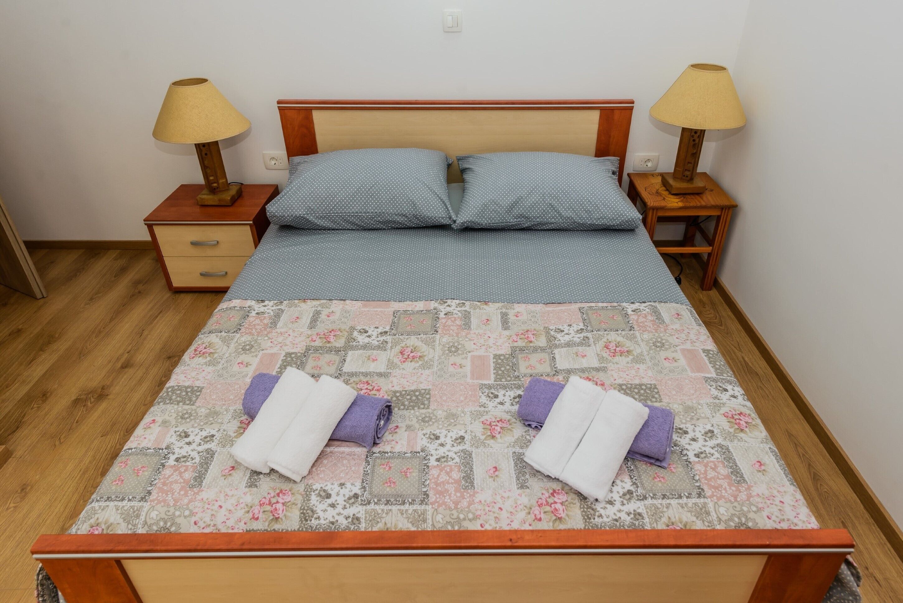 A neatly made bed with a floral quilt, two pillows, and two towels on the bed.