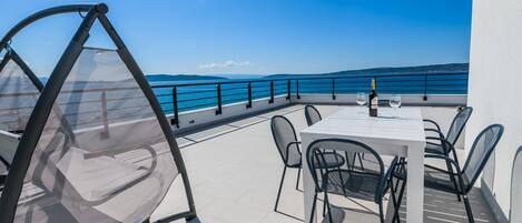 A terrace with a white table and chairs, overlooking a body of water and distant hills.