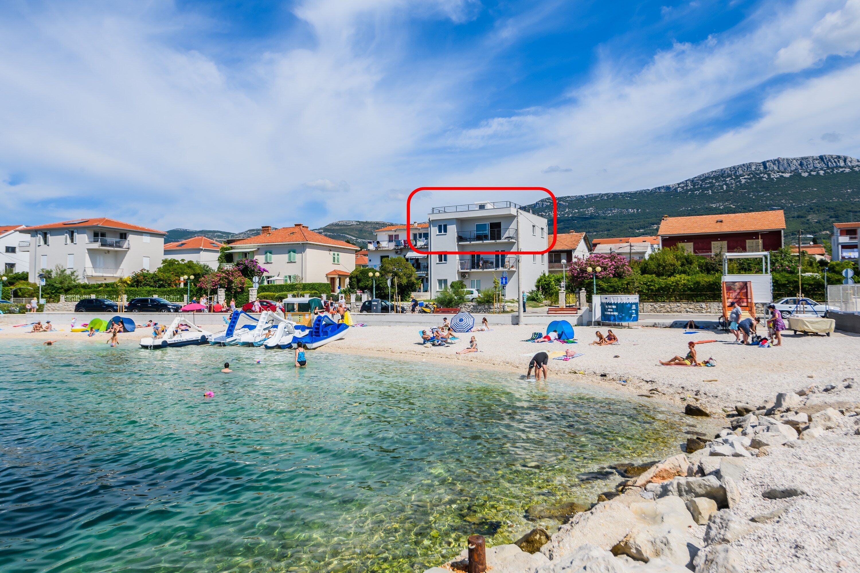 Un poble costaner amb aigües cristal·línes, platja i edificis amb teulades vermelles.