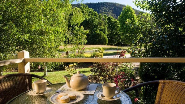 Ein Tisch mit Teekanne, Tassen und Gebäck auf einem Balkon mit Blick auf einen Garten, Bäume und eine Hügellandschaft.