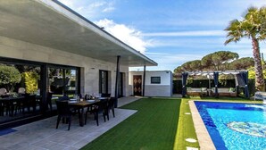 Et moderne hus med swimmingpool, en terrasse med bord og stole, samt et overdækket udendørs siddeområde.