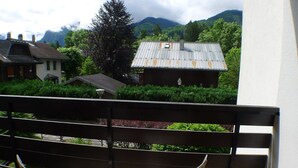 Un balcone con due poltrone bianche, vista su una montagna e un edificio con tetto in metallo.