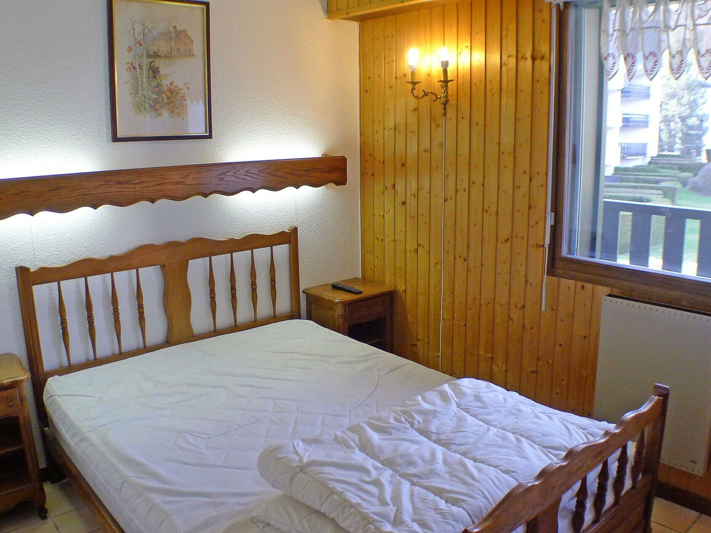 A wooden bed with a white mattress in a room with wooden walls and a window.