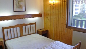 Un letto di legno con materasso bianco in una stanza dalle pareti in legno e una finestra.