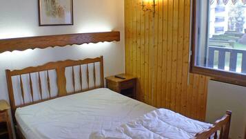 A wooden bed with a white mattress in a room with wooden walls and a window.
