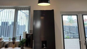 Uma cozinha com geladeira preta moderna, uma luminária pendente e uma janela com vista para um quintal.