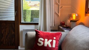 A cozy room with a view of a mountain, a red pillow with "SKI" on it, and a table with a candle.