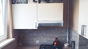 Ett kompakt kök med vita skåp, en gasspis, en kaffemaskin och ett fönster som släpper in naturligt ljus.