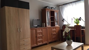 Ett vardagsrum med ett träskåp, en tv, ett skrivbord med en stol och en krukväxt.
