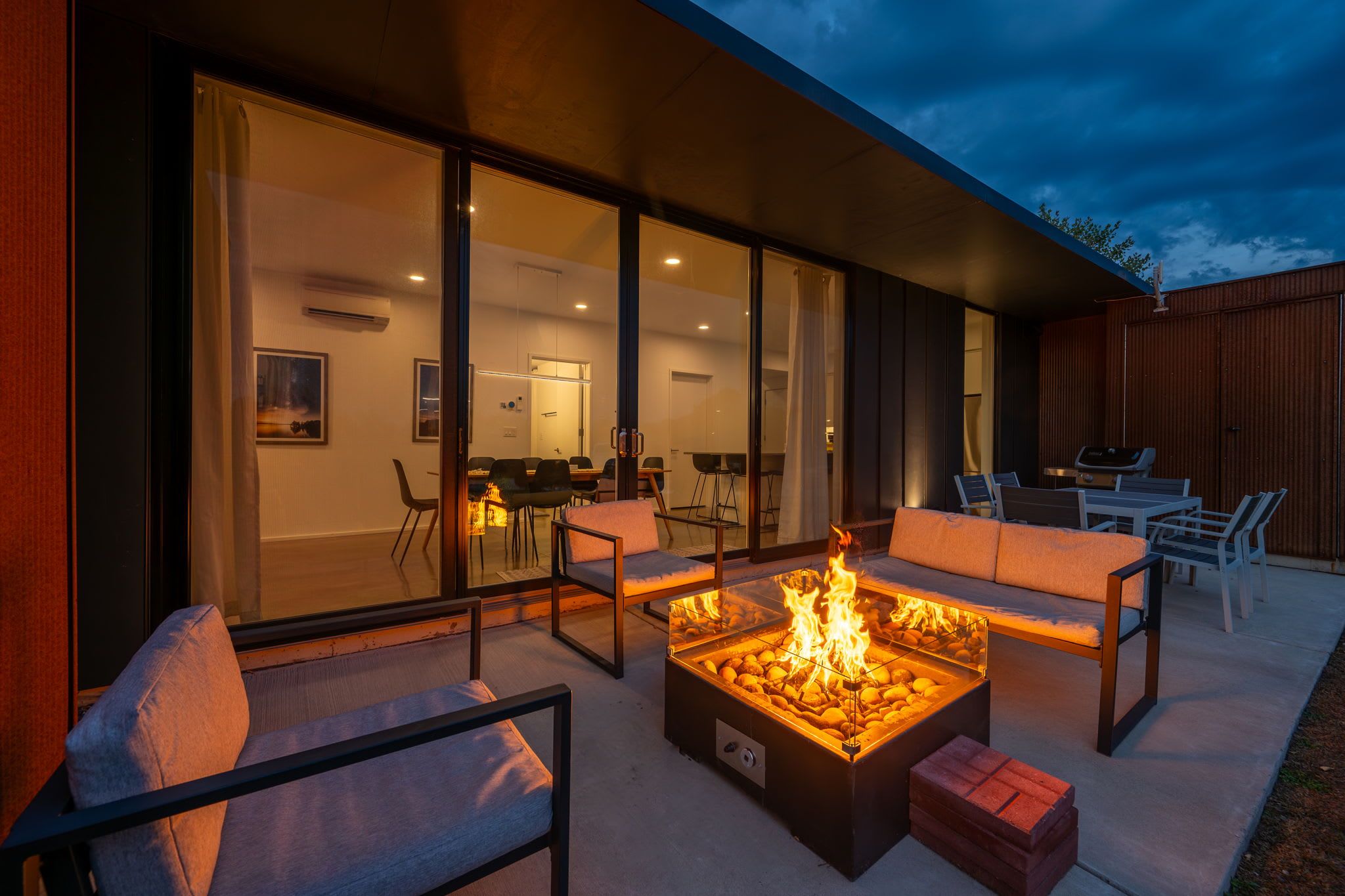 Une terrasse extérieure dotée d’un foyer, de sièges et offrant une vue sur l’intérieur.
