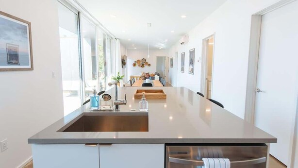 A modern kitchen with a central island, large windows, and a view of the dining area.