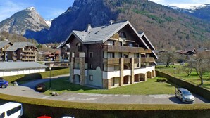 A mountain lodge with a prominent peak in the background, featuring a central building with balconies and a parking area in the foreground. - 2-room apartment with pets allowed, balcony and garage (Samoëns)