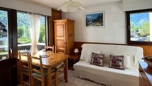 A cozy room with a wooden dining table, chairs, a sofa with patterned cushions, a cabinet, and a painting on the wall. - 2-room apartment with pets allowed, balcony and garage (Samoëns)
