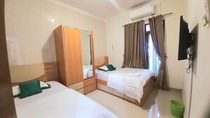 Una camera d'albergo con due letti singoli, un armadio, uno specchio, una TV a parete e una finestra con tende.