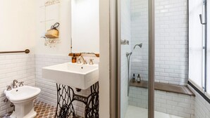 A bathroom with a white sink, a pedestal basin, a glass shower enclosure, and a white tiled shower area.