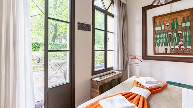 A room with a bed, a window with a view of greenery, a towel rack, and a framed artwork.